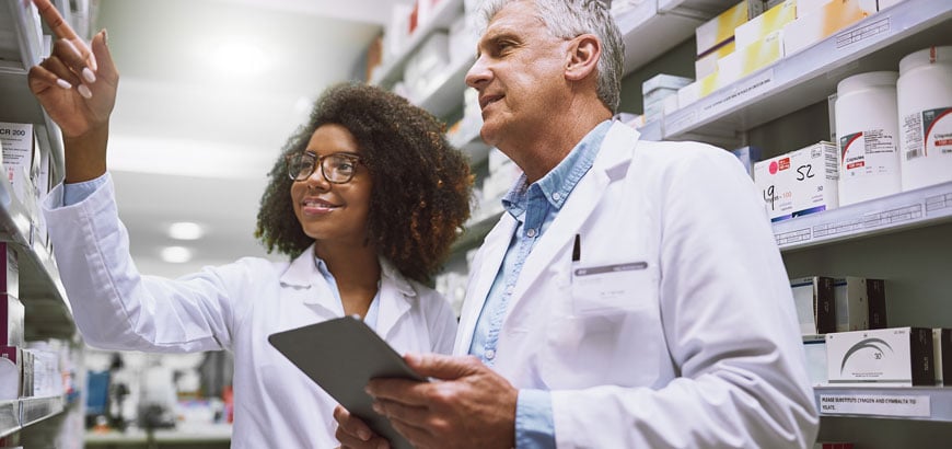 <span>Image of two focused pharmacists walking around and doing stock inside of a pharmacy</span>