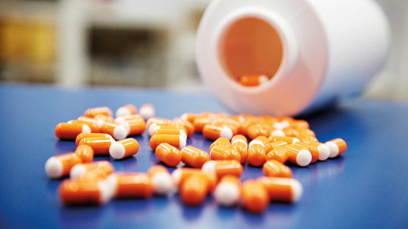 Several pills lying on a table in front of an open pill bottle