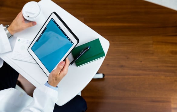 Overhead image of a healthcare worker using an iPad and holding a hot coffee