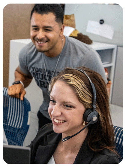 Two coworkers smile while one is wearing a telephone headset