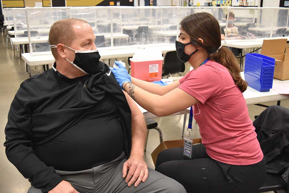 A woman administering a COVID-19 vaccine to a man sitting in a chair