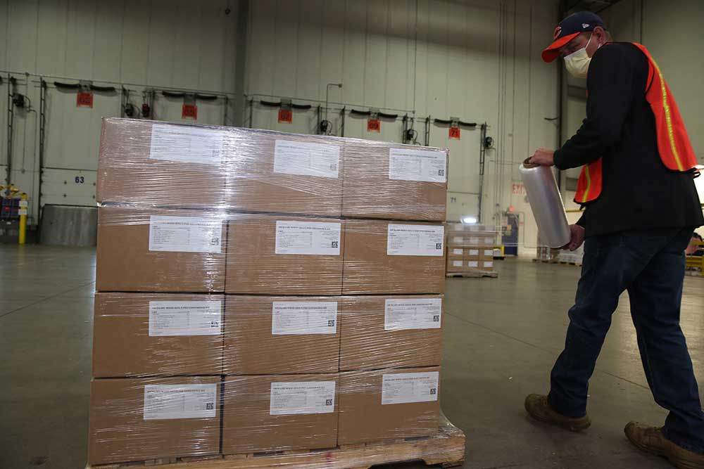 A worker wrapping a stack of boxes on a pallet with plastic shrink wrap