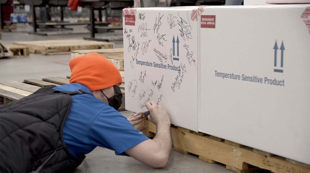 Workers signing a box of Johnson and Johnson COVID-19 vaccines