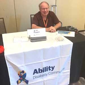 Terry Black sitting at a table at a conference with the Ability ERG logo on it.